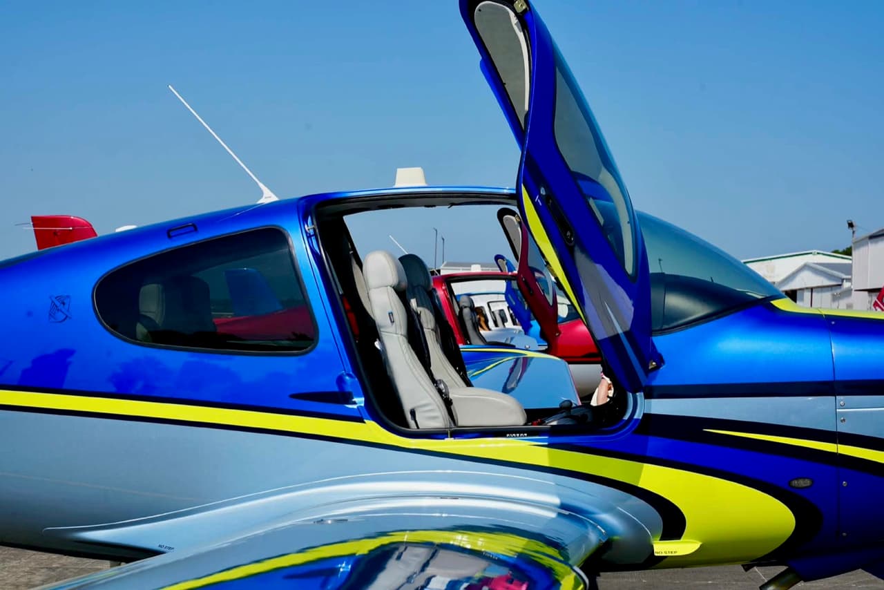 The open gull-wing door of a blue and lime Cirrus, showing the leather seats and dual controls inside